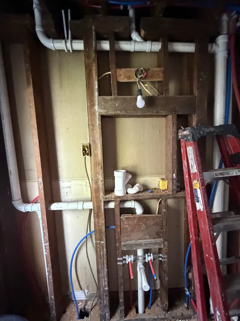 PVC drain, waste and vent replacement piping exposed in open wall framing beside a red ladder.