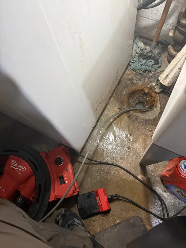 Drain cleaning cable machine next to an open floor cleanout