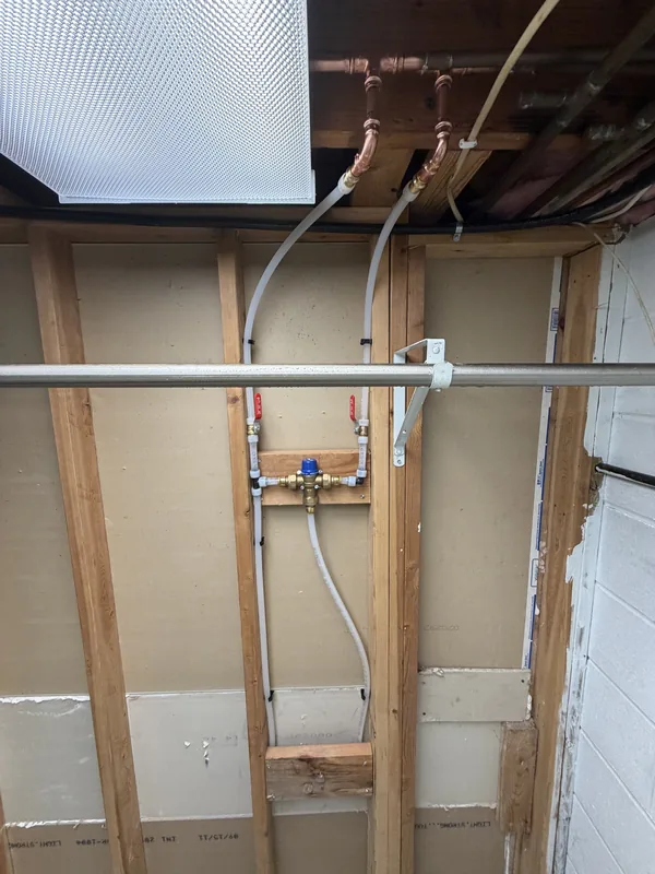 Mixing valve and water supply lines roughed in behind a wall during a remodel