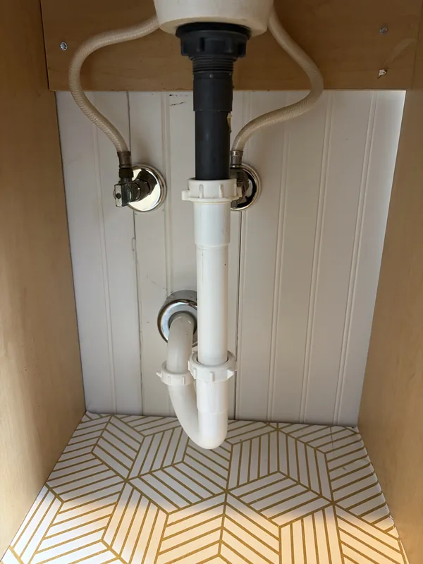 Vanity sink drain trap and supply valves installed under a bathroom cabinet
